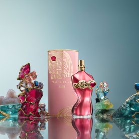 Jean Paul Gaultier La Belle Rosea Eau de Parfum in pink bottle and box, surrounded by colourful crystal decorations on reflective surface