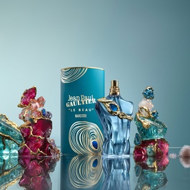 Jean Paul Gaultier Le Beau Narcisse Eau de Parfum bottle with teal cylindrical box, gold cap, surrounded by colourful sculptural accents