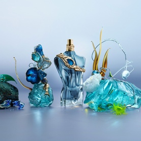 Jean Paul Gaultier Le Beau Narcisse Eau de Parfum bottle in blue glass with gold cap, styled with sculptural blue resin ocean-themed decorative pieces