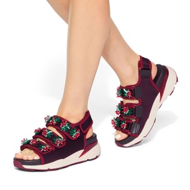 Model wearing Kurt Geiger London red chunky sandals with multicoloured floral embellishments, velcro straps, and white platform sole.