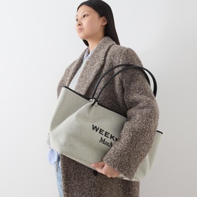 Model carrying Max Mara Weekend Getto Canvas Logo Tote Bag in black canvas with silver hardware, styled with a grey wool coat and jeans