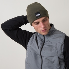 Model with North Face Dock Worker Logo Beanie Hat in New Taupe Green, ribbed knit with logo badge, styled with grey gilet and black base layer