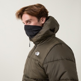 Model wearing North Face casual jacket in New Taupe Green, quilted puffer style with hood, paired with black face covering.