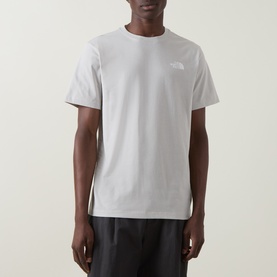 Model wearing North Face Evolution Box Logo Back Graphic T-Shirt in Cumulus Cloud, crew neck, short sleeves, styled with dark trousers.