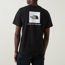 Model wearing The North Face Evolution Box Logo Back Graphic T-Shirt in black, showing white square logo and "Never Stop Exploring" slogan on back.