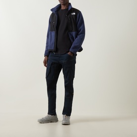 Model wearing North Face Evolution Box Logo Back Graphic T-Shirt in black, styled with navy fleece jacket, dark cargo trousers and grey trainers.