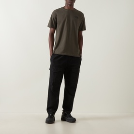 Model wearing North Face Yosemite Oak Logo Back Graphic T-Shirt in New Taupe Green, styled with black cargo trousers and dark trainers.