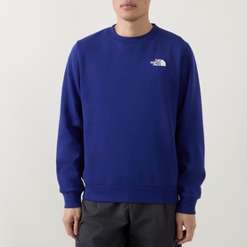 Model wearing North Face Bold Blue crew neck sweatshirt with small chest logo print, styled with dark trousers.