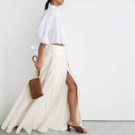 Model wearing Reiss white maxi skirt with front split, styled with a white cropped shirt, brown heels and small tan bag.