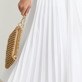 Model carrying a gold beaded chain-handle clutch bag, styled with a white pleated Reiss dress