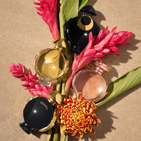 Paco Rabanne Olymp&eacute;a Elixir Eau de Parfum Intense and fragrance bottles arranged with tropical pink ginger flowers and orange chrysanthemum on sandy