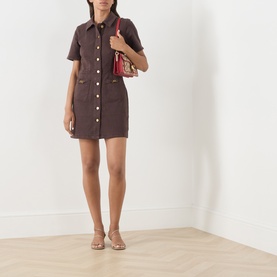 Model wearing Paige Rich Chocolate mini shirt dress with short sleeves and button front, styled with nude heels and small red shoulder bag.