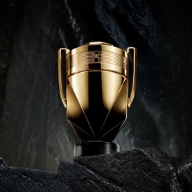 Paco Rabanne Invictus Elixir Parfum in gold trophy-shaped bottle with black faceted base, displayed on dark stone surface
