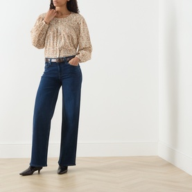 Model wearing Paige Straight Jeans in Basillica dark blue denim with belt, styled with a floral top and black heeled mules.