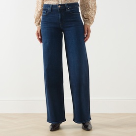 Model wearing Paige straight jeans in Basillica dark blue denim, wide-leg silhouette, styled with a floral blouse and black shoes.