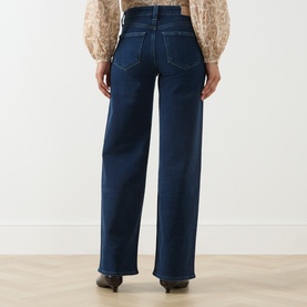 Model wearing Paige straight jeans in Basillica dark blue denim, rear view, styled with a floral blouse and black heeled boots