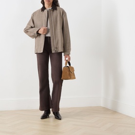 Model wearing Paige Rich Chocolate wide leg jeans, styled with a taupe bomber jacket and black ankle boots, carrying a tan top-handle bag.