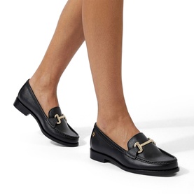 Model wearing black leather loafers with gold-tone snaffle bit hardware and low block heel