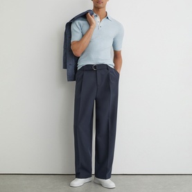 Model wearing Reiss soft blue short-sleeve polo shirt, styled with navy wide-leg trousers, white trainers and navy blazer over shoulder.