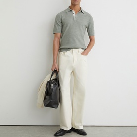 Model wearing Reiss soft sage knitted polo shirt, styled with cream wide-leg jeans, carrying a black holdall bag