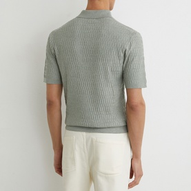 Model wearing Reiss soft sage textured knit polo shirt, short sleeves, styled with white trousers, back view.
