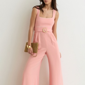 Model wearing Reiss pink wide-leg jumpsuit with square neckline, thick straps and circular belt buckle, styled with a woven clutch bag.