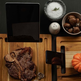 Tramontina brown acacia wood chopping board with tablet stand slot, styled with steak, mushrooms, salt and pepper on dark surface