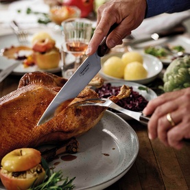 Tramontina black carving knife slicing roast turkey on a festive table set with side dishes and seasonal accompaniments