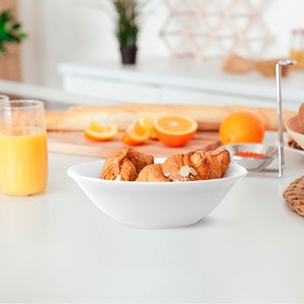 White ceramic bowl filled with croissants on a kitchen counter, styled with orange juice and fresh oranges in the background.
