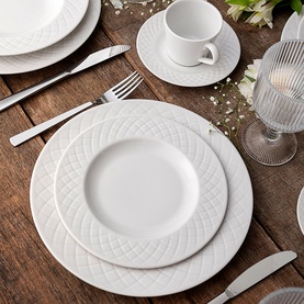 White embossed quilted dinnerware set styled on wooden table with cutlery and glassware, including dinner plate, side plate, cup and saucer