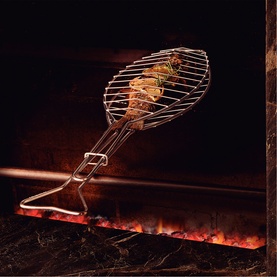 Tramontina stainless steel fish griddle basket held over open flames, with grilled fish visible inside the wire cage design