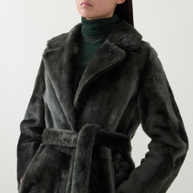 Model wearing Yves Salomon Long Belted Grey Shearling Coat with notched lapel and self-tie belt, styled with a dark green roll-neck