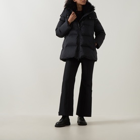 Model wearing Yves Salomon A-Line Down Jacket in black with removable shearling collar and hood, styled with black flared trousers and chunky loafers