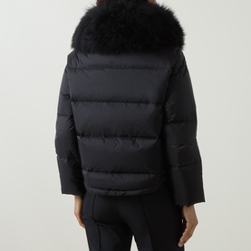 Model wearing Yves Salomon Cropped Down Jacket in black, rear view, with voluminous shearling collar and quilted panels, styled with black trousers.