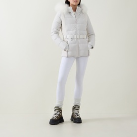 Model wearing Yves Salomon Fur-Trim Padded Ski Jacket in Mont Blanc with fur-trimmed hood and matching belt, styled with white leggings and chunky