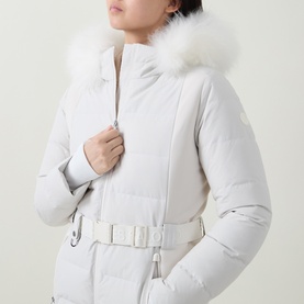 Model wearing Yves Salomon Fur-Trim Padded Ski Jacket in Mont Blanc with white fur hood trim, high neckline, and belted waist