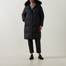 Model wearing Yves Salomon black longline puffer coat with faux fur trim hood, styled with dark cropped trousers and black loafers.