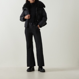 Model wearing Yves Salomon Salopettes Flared-Leg Ski Trousers in black, styled with a black puffer jacket with fur collar and chunky loafers.