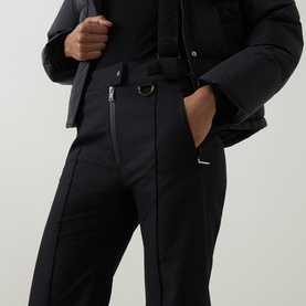 Model wearing Yves Salomon Salopettes Flared-Leg Ski Trousers in black with adjustable logo jacquard suspenders, styled with a dark jacket.
