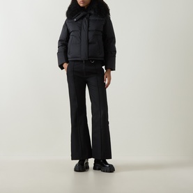 Model wearing Yves Salomon Salopettes Flared-Leg Ski Trousers in black, styled with a black puffer jacket and chunky black boots.