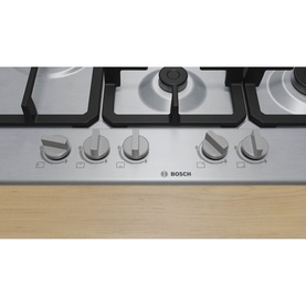 Bosch silver gas hob with five burners, cast iron pan supports, and five control knobs, built into a wooden worktop.