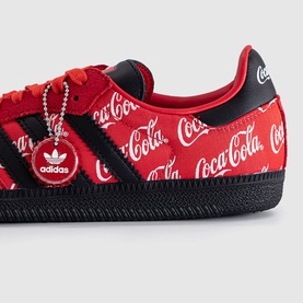 Adidas trainer in red Coca-Cola print with black three-stripe overlay, black sole, and Adidas charm detail.