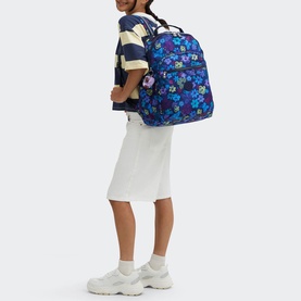 Model carrying Kipling Seoul Lap Backpack in Dark Flwr Stamp, blue floral print, worn as backpack with adjustable straps, styled with white skirt and