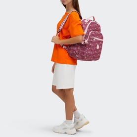 Model carrying Kipling Seoul Lap Backpack in U R Great Prt, pink floral print, worn as backpack with adjustable straps, styled with orange tee and