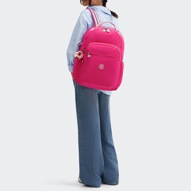 Model carrying Kipling Seoul Lap Backpack in Intense Rose; large nylon backpack with gold-tone zip pulls and branded monkey charm, worn with blue