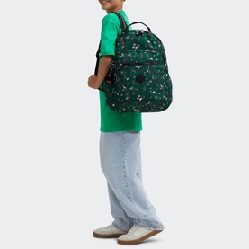 Model carrying Kipling Seoul Lap Backpack in Soccer Prt print, worn on back by child in green tee and wide-leg jeans.