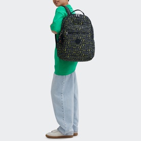 Model carrying Kipling Seoul Lap Backpack in Lets Play Prt print, worn on back, styled with green sweatshirt and light blue jeans.