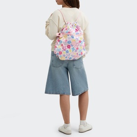 Model carrying Kipling Supertaboo Gym Bag in Flower Stamp print, worn as drawstring backpack, styled with cream jumper and wide-leg jeans.
