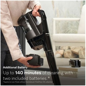 Miele cordless stick vacuum in black held by model, with additional battery pack visible, highlighting 140-minute runtime with two batteries