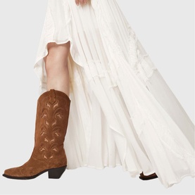 Model wearing All Saints Dorina Asymmetric Skirt in antique white with high-low hemline, styled with tan suede cowboy boots.